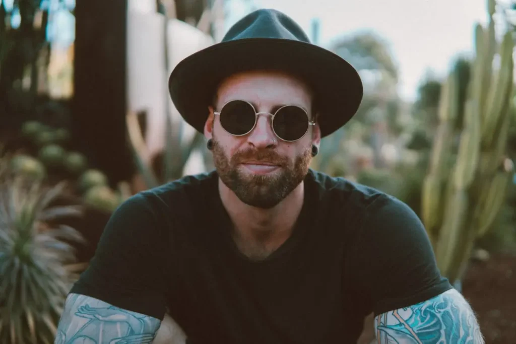 Man with sunglasses, hat and beard sitting outdoors