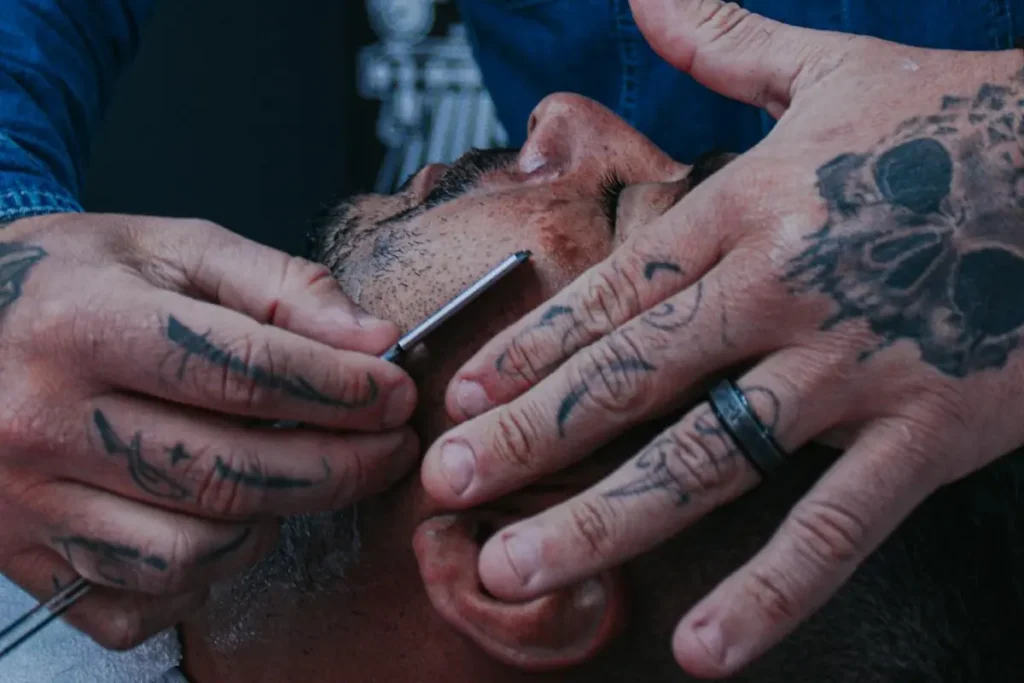 Hands of one man shaving another man's beard