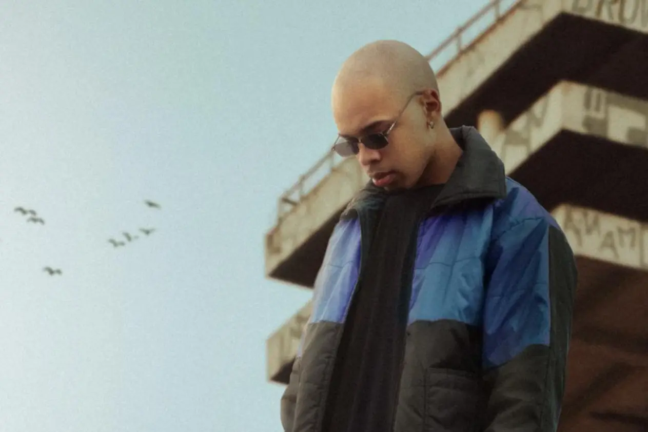 a man with a shaved head and glasses standing on an outdoor