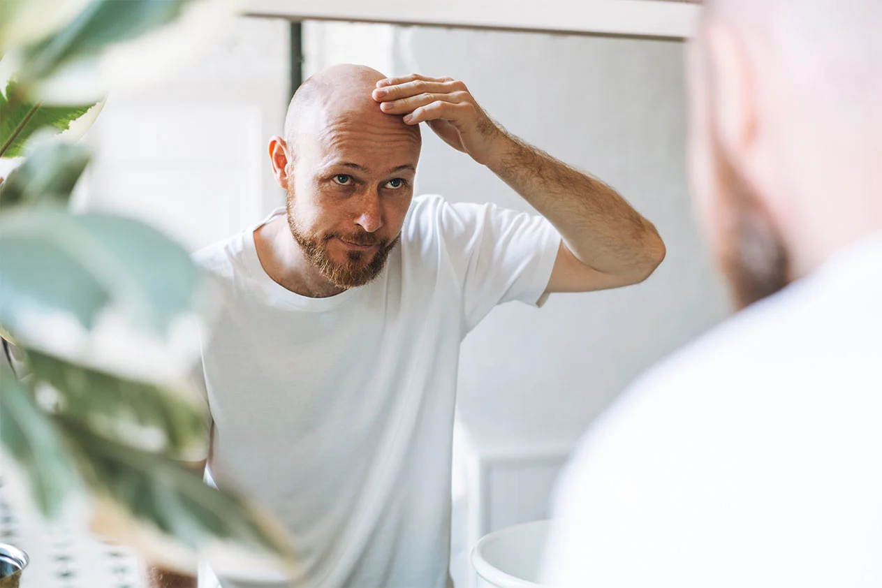 a man applying a product to his shaved head in front of a mirror