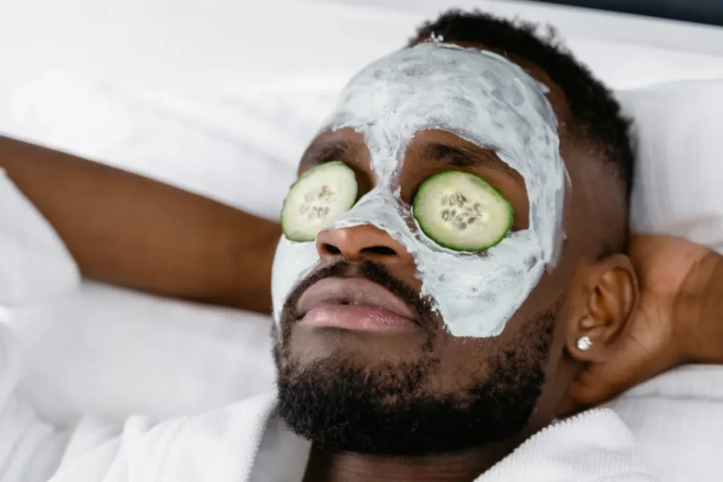 A bearded man lying in a spa with a mask and cucumbers