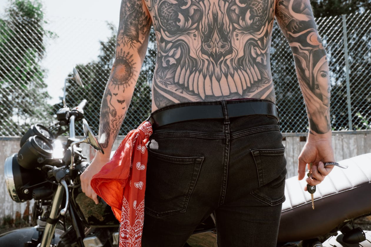 back of a man with tattoos walking toward his motorcycle