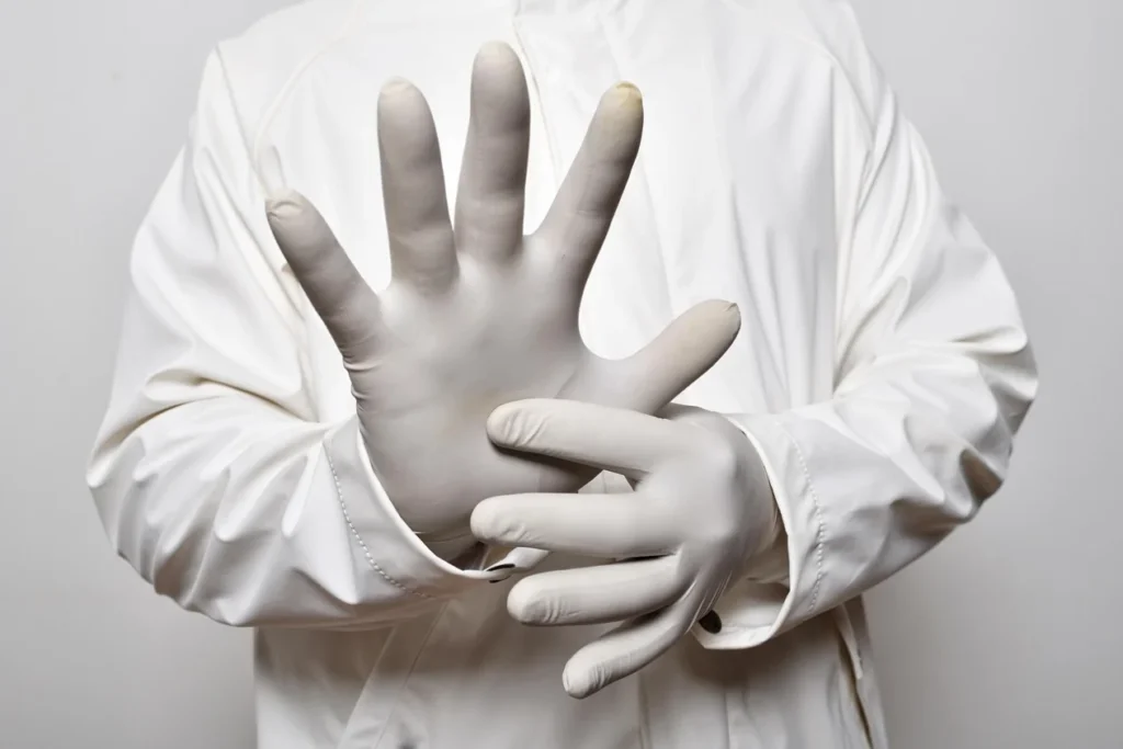 You see part of a person wearing a white coat showing their surgical gloves.