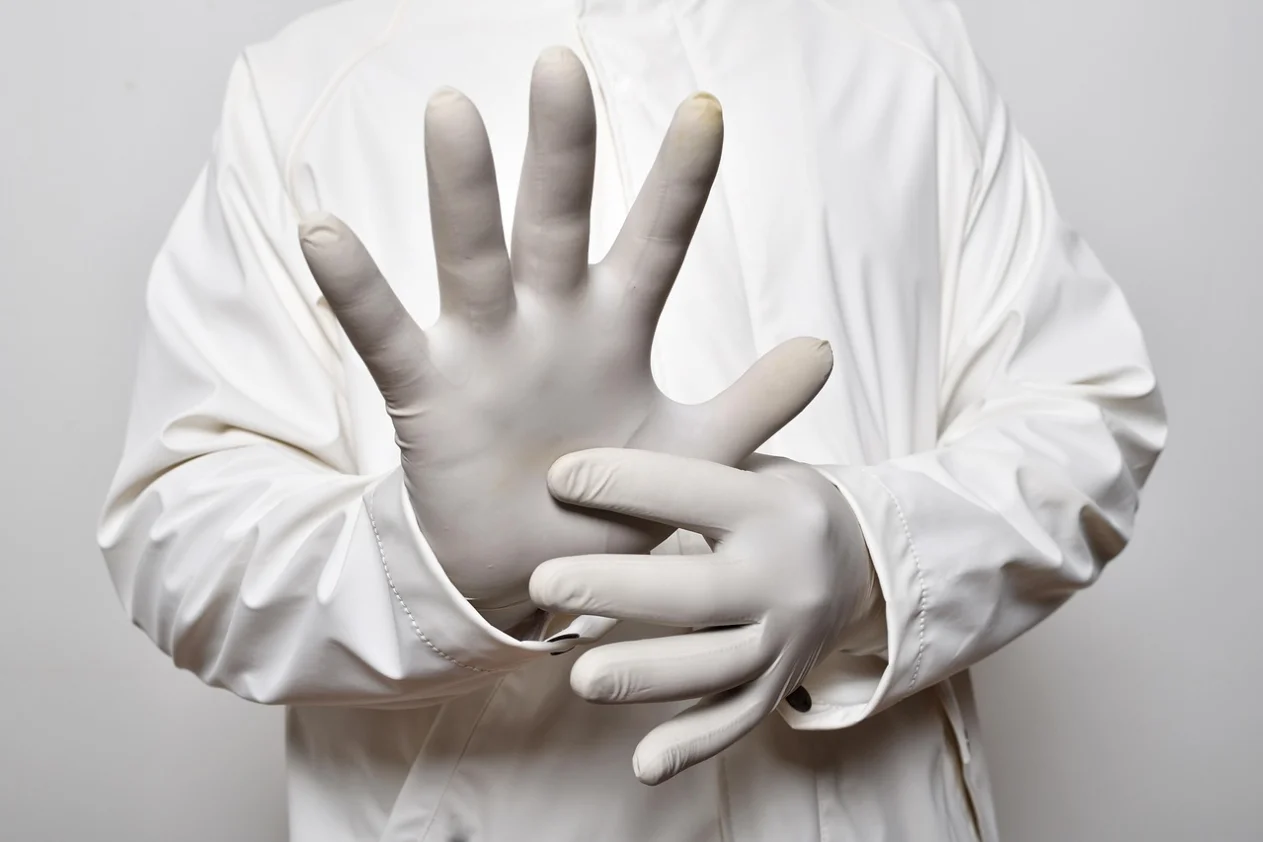 You see part of a person wearing a white coat showing their surgical gloves.