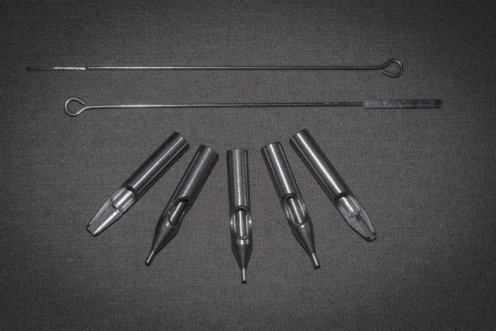 2 needles and 5 nozzles for tattooing on a gray surface.